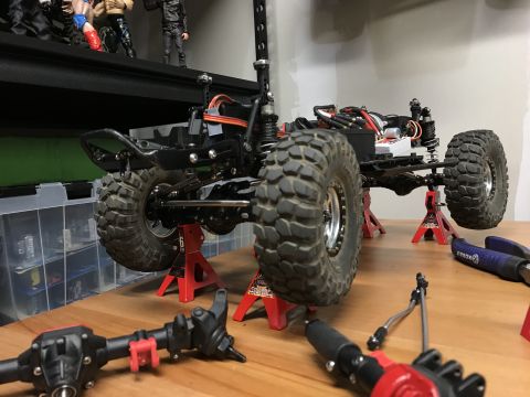 1989 Ford Bronco - Remote control car chassis with large tires is elevated on jack stands, with its front axle disassembled on the table.