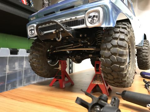 1989 Ford Bronco - A blue Chevrolet pickup truck is elevated on red jack stands, revealing its front suspension and oversized tires.