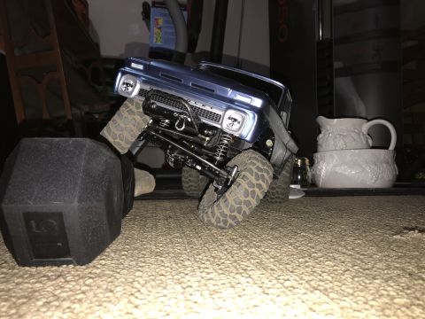 1989 Ford Bronco - RC truck with detailed grille and suspension is positioned on carpet near a dumbbell.