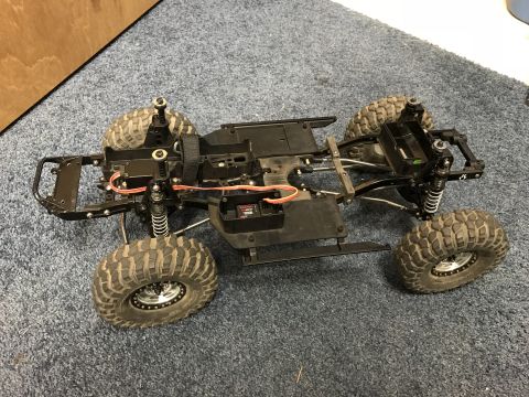 1989 Ford Bronco - The chassis of a remote control car, showing its suspension and large off-road tires, sits on a carpeted surface.