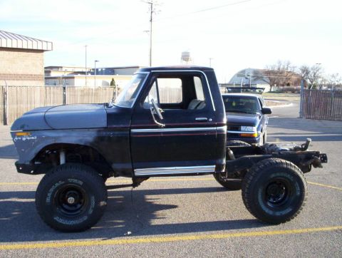 1978 Ford Bronco - Side profile of a lifted late-1970s Ford project truck with the entire rear body removed, exposing the bare frame behind the black cab. The…