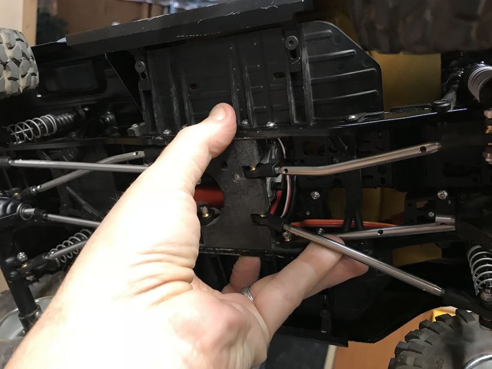Hand holding the underside of a remote control car chassis, showing suspension and drive shafts