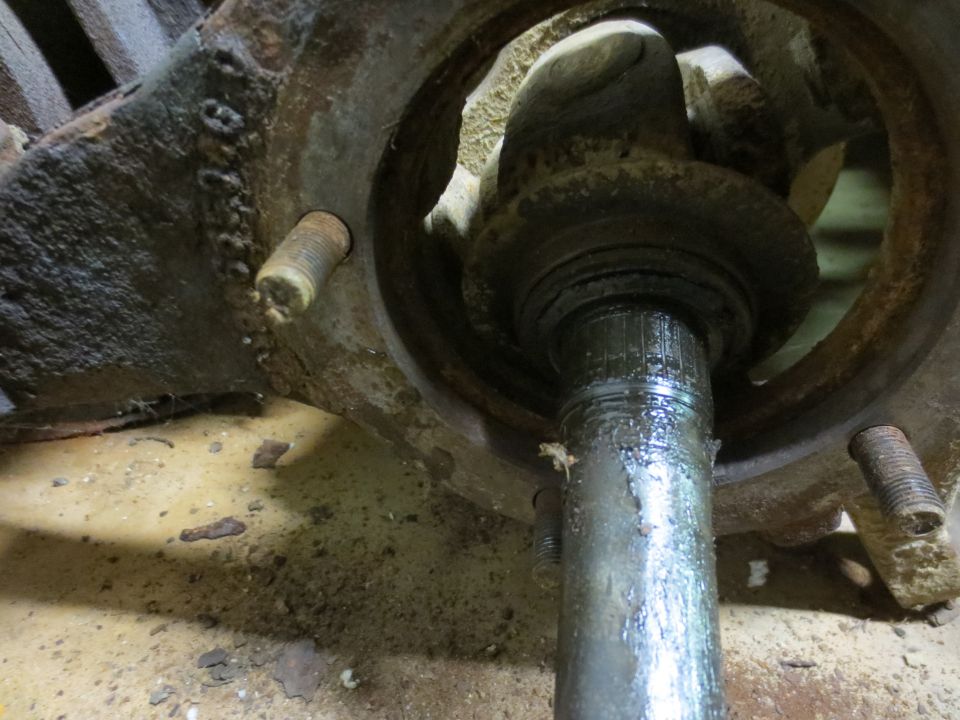 Close-up of a rusty, greased axle shaft and hub assembly.