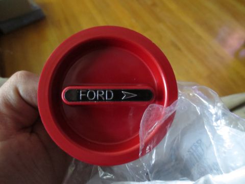 1967 Ford F-250 - A red circular part with a Ford emblem is held in a hand, partially covered by plastic packaging.