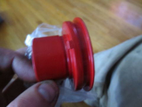 1967 Ford F-250 - A red pulley part is held in a hand, with a blurred background of wood flooring and fabric.