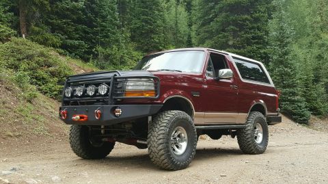 1996 Ford Bronco - This modified Ford Bronco is parked on a dirt road surrounded by trees.