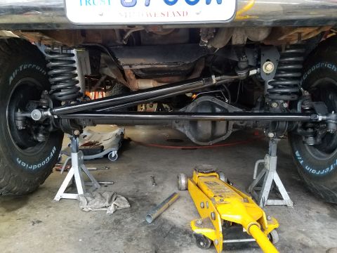 1995 Ford Bronco - The undercarriage of a vehicle is shown, supported by jack stands, with visible suspension components and tires.