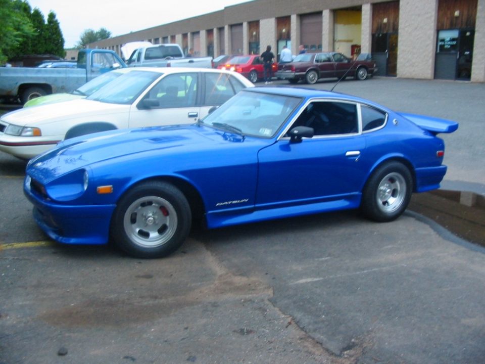 Blue Datsun Z coupe in side profile on mag wheels outside a commercial garage