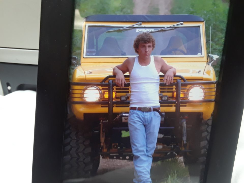 Yellow 1978 Ford Bronco with a black grille guard and a man leaning on it