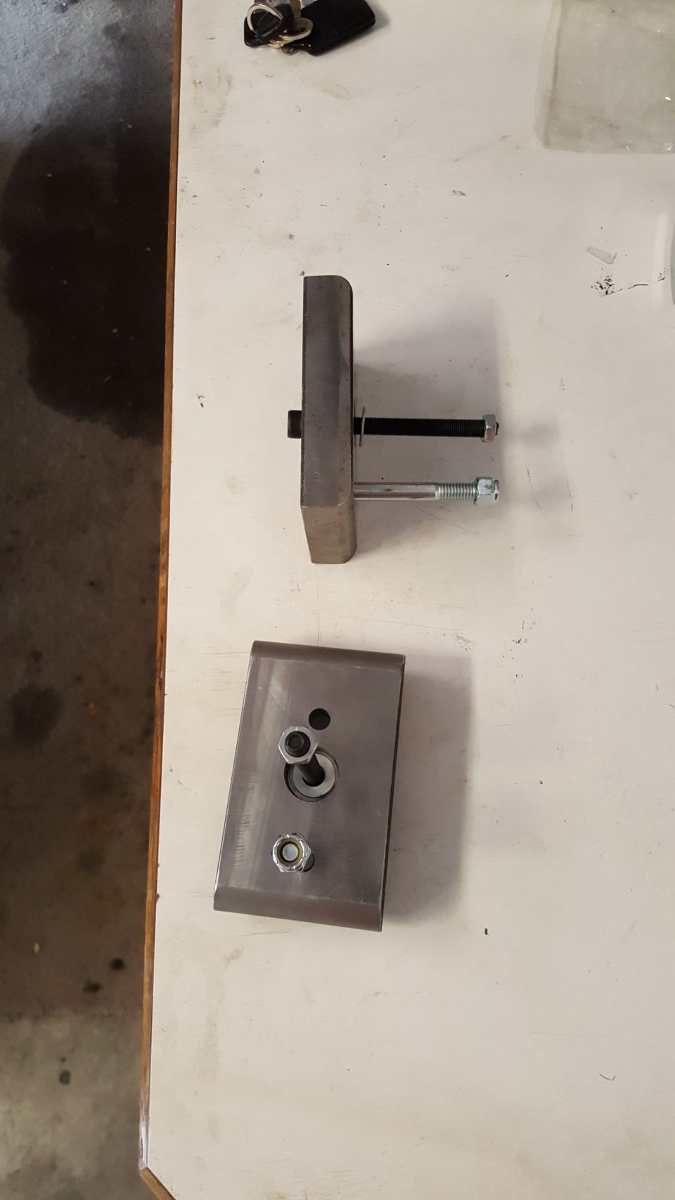 Two metal fabricated parts with bolts and nuts on a white surface.