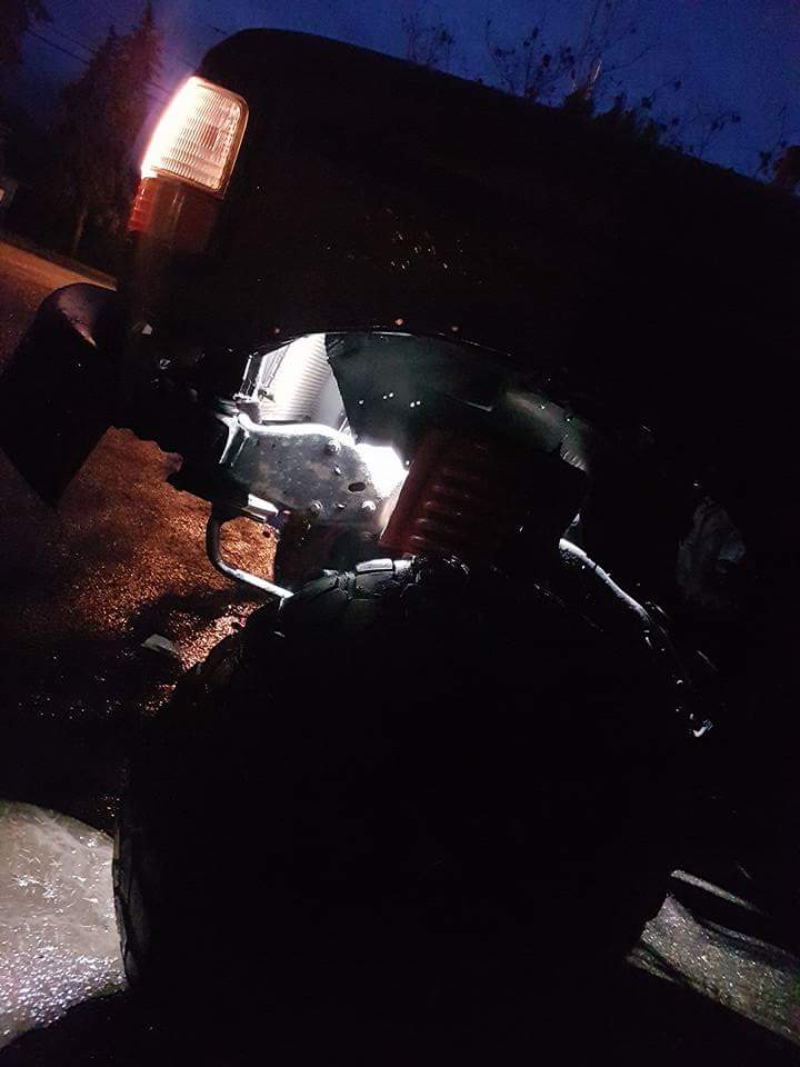 Rear passenger side of a dark pickup truck at night, showing suspension and tire.