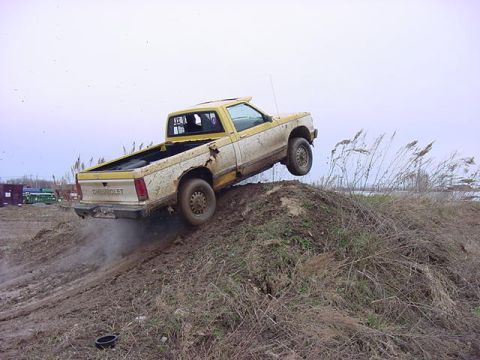 1994 Ford Bronco - A Chevrolet pickup truck navigates a muddy incline, kicking up dirt as it goes.