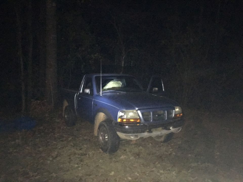 Blue 1998 Ford Ranger pickup truck parked in a wooded area at night, driver's door open.