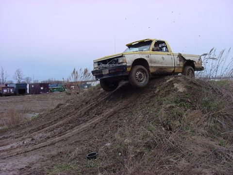 1994 Ford Bronco - A damaged pickup truck navigates a steep, muddy incline.