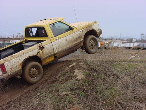 1994 Ford Bronco - This pickup truck is navigating a challenging muddy terrain, with its front passenger-side wheel lifted off the ground.