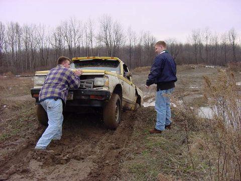 1994 Ford Bronco - Two men attempt to free a vehicle stuck deep in the mud on an overcast day.