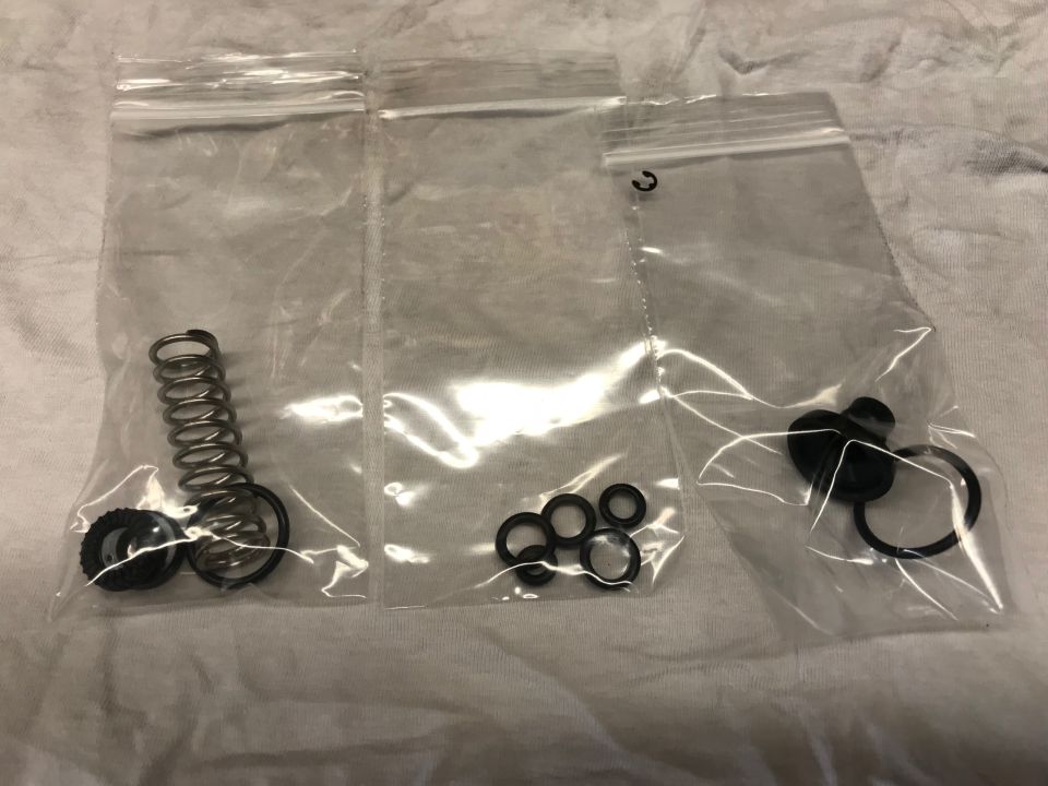 Three plastic bags with small parts like springs and O-rings on a white surface.