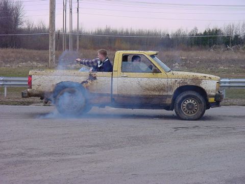 1994 Ford Bronco - A yellow pickup truck is shown from the side, performing a burnout and kicking up smoke.