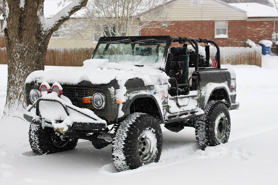 Snow-covered 1972 Ford Bronco with aftermarket lights and large tires.