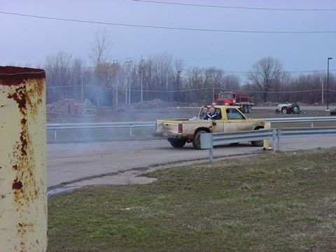1994 Ford Bronco - Pickup truck with passengers in the bed drives on a dirt track, with other vehicles visible in the distance.
