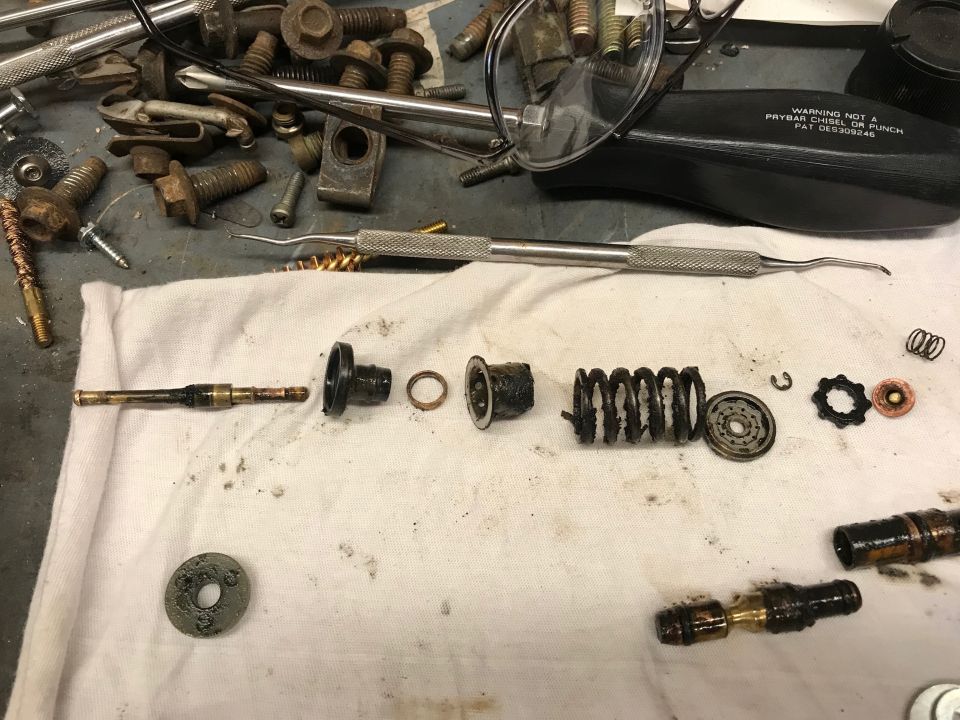 Disassembled mechanical parts, springs, washers, tools, and fasteners on a white cloth.