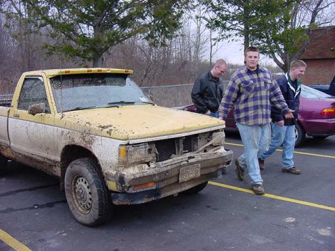 1994 Ford Bronco - A dirty pickup truck is parked in a lot with people walking past.