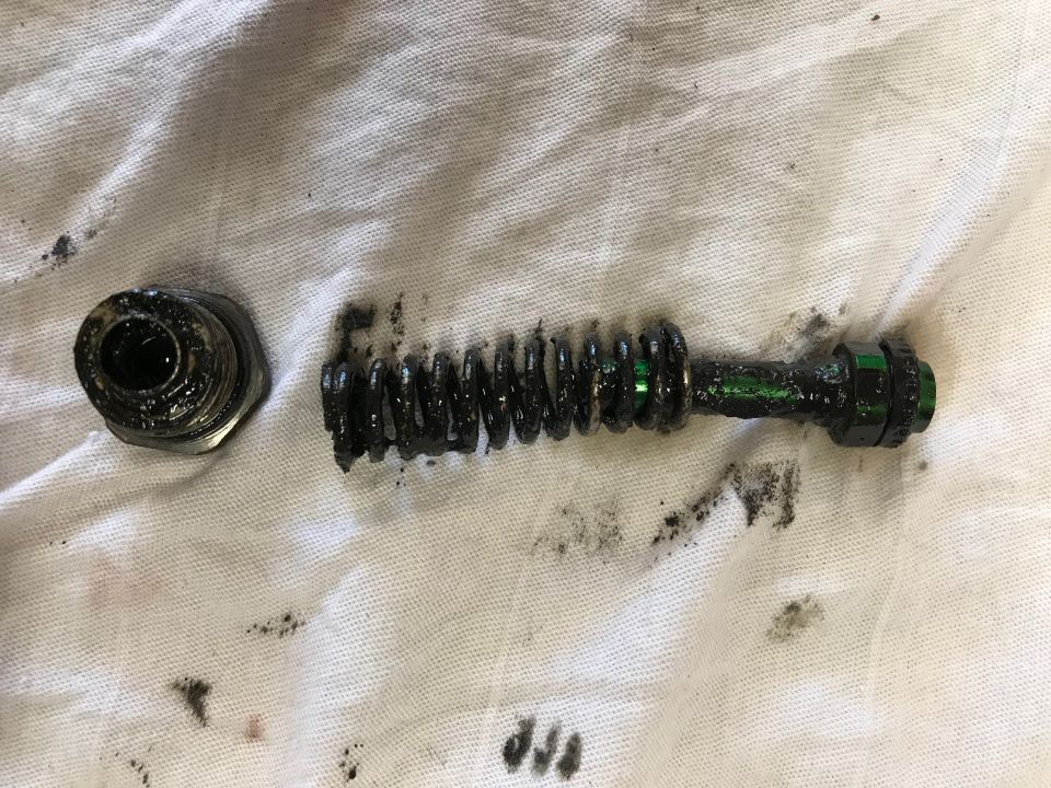 Disassembled automotive part with spring and threaded component covered in grease on white cloth.