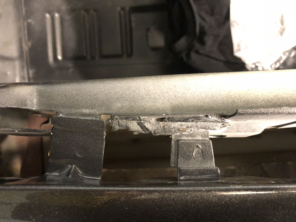Damaged metal trim with black plastic clips on a vehicle.