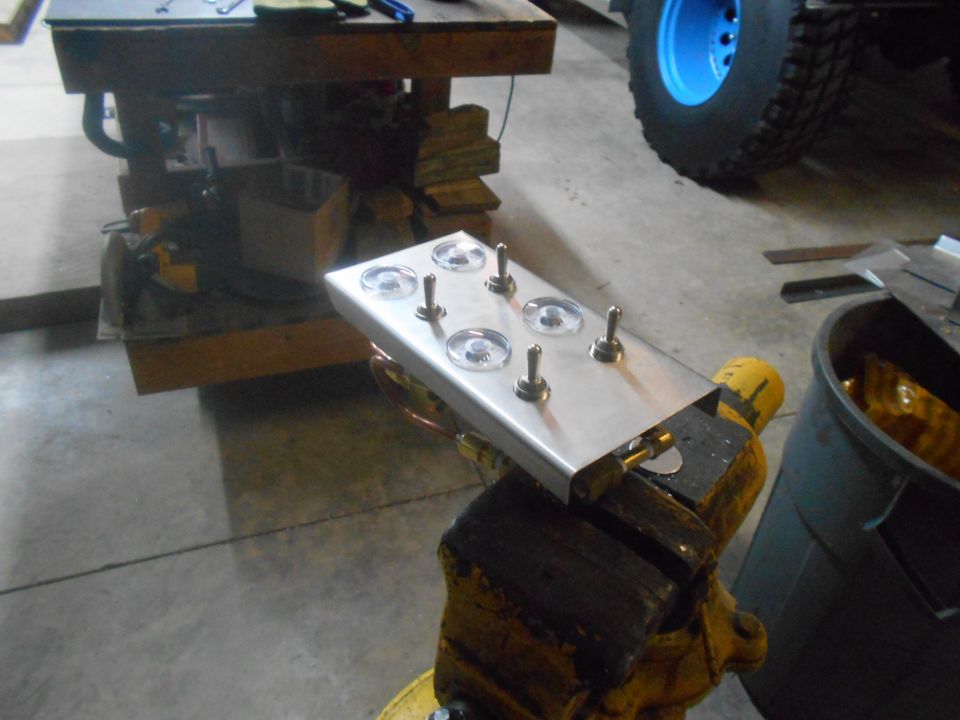 Custom switch panel with six toggle switches clamped in a vise, blue wheel in background.