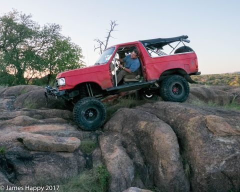 1989 Ford Bronco - A red SUV navigates a rocky terrain, its off-road capabilities.