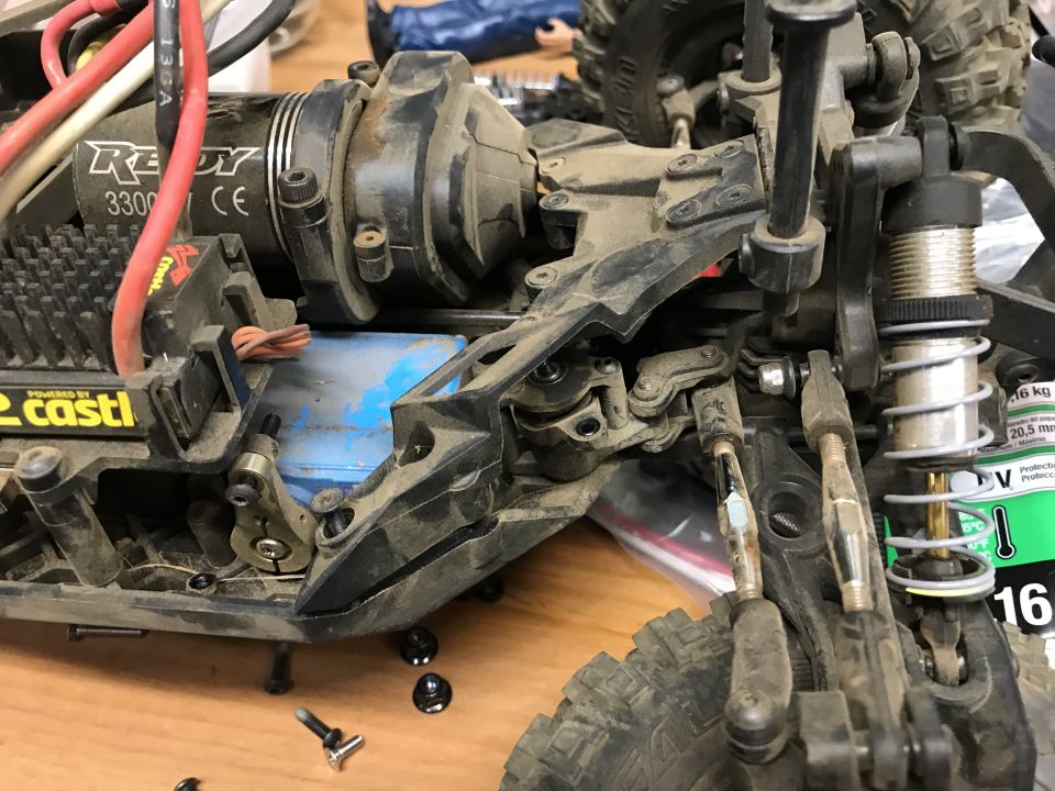RC car chassis showing motor, suspension, and battery pack. Some screws are loose on the surface