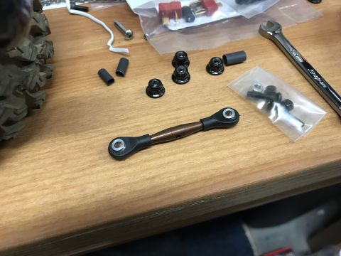 1989 Ford Bronco - Various parts for an RC car, including a linkage, nuts, and a wrench, are laid out on a table.