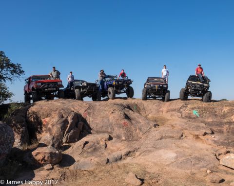 1989 Ford Bronco - A group of off-road enthusiasts and their customized vehicles pose on a rocky terrain.