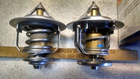 2008 Hyundai Accent - Two automotive thermostats are shown side-by-side, with visible text on a wooden backing.