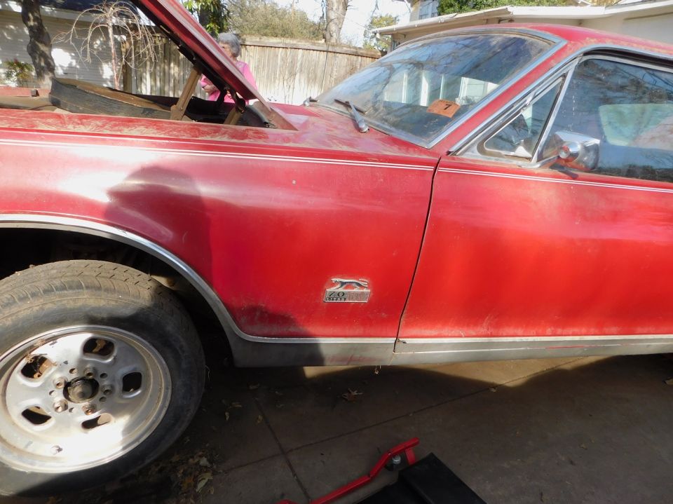 Red 1968 Mercury Cougar side view, hood open, showing engine bay. Chrome trim and fender emblem visible