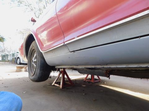 1968 Mercury Cougar - The underside of a red vehicle is supported by jack stands, revealing its rusty undercarriage.