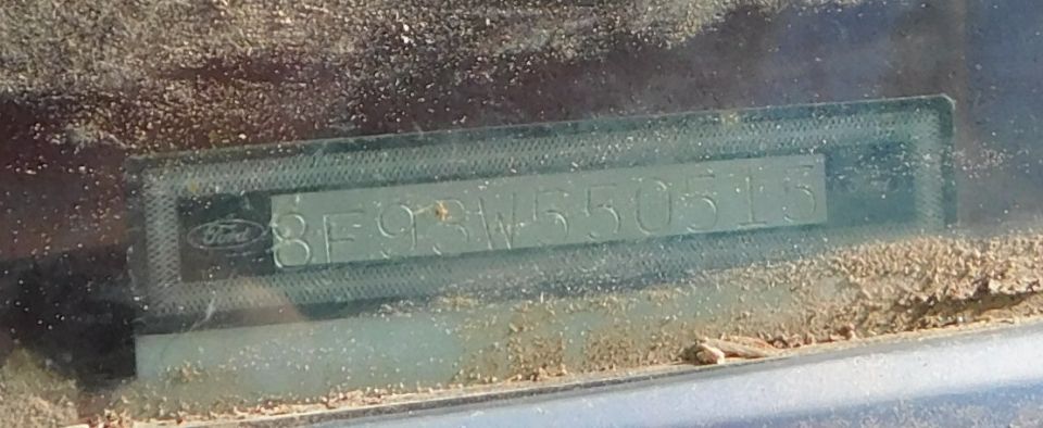 Ford dash-mounted VIN plate seen through a dusty windshield, number partly legible