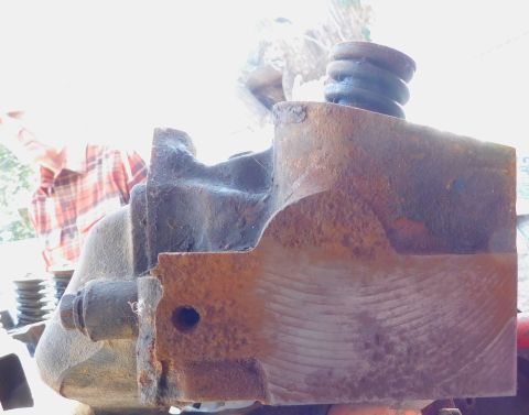 1968 Mercury Cougar - A rusty brake master cylinder with a coiled spring is shown, with a person in a plaid shirt blurred in the background.