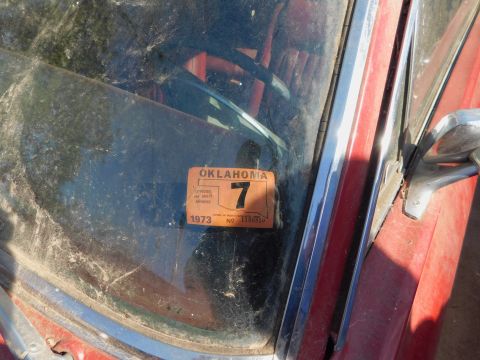 1968 Mercury Cougar - A close-up view of a dusty Oklahoma 1973 vehicle registration sticker adhered to the windshield of a red car.