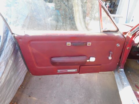 1968 Mercury Cougar - The interior of a car door shows a red vinyl panel with a pull handle and armrest.