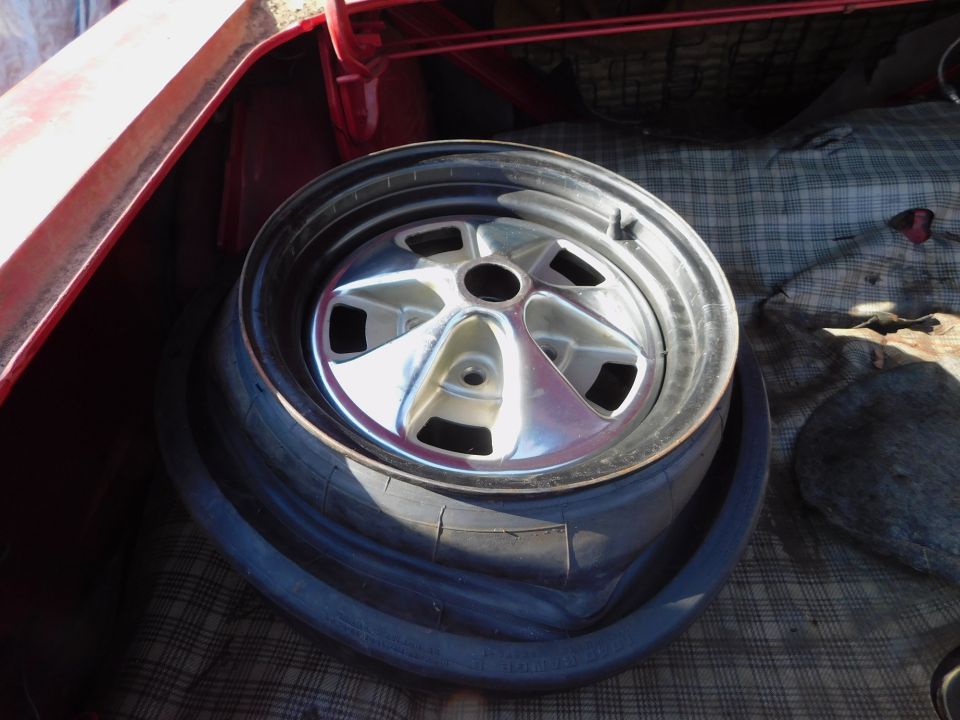 Spare tire and chrome wheel in red car trunk with plaid lining