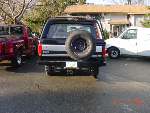 1995 Ford Bronco rear view with spare tire, parked next to a red pickup truck and a white van