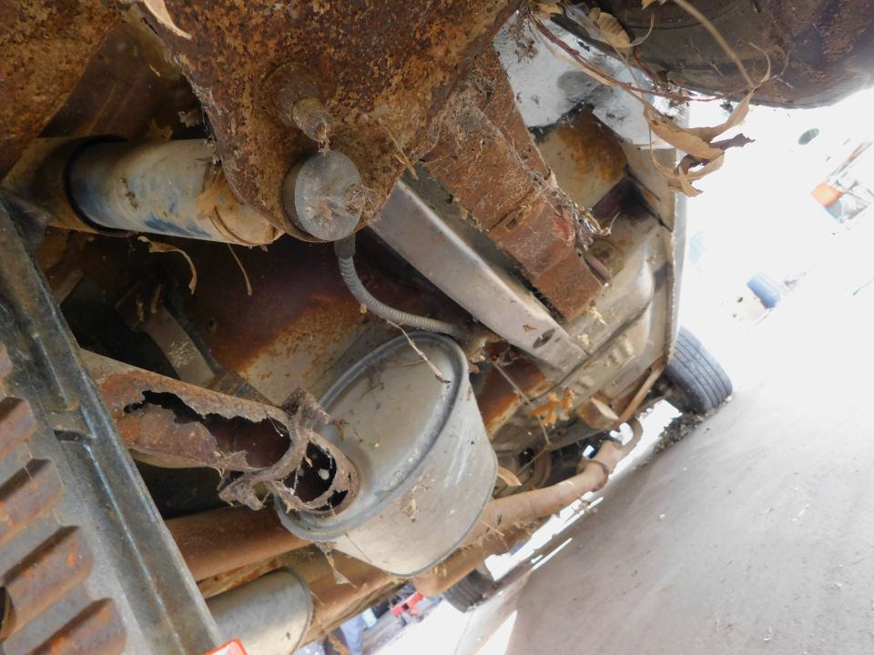 Heavily rusted vehicle undercarriage with exhaust pipe, muffler, and suspension components visible