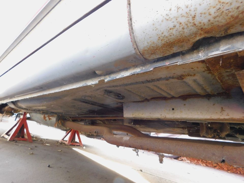 Underside of a car on red jack stands, showing rusty frame and exhaust