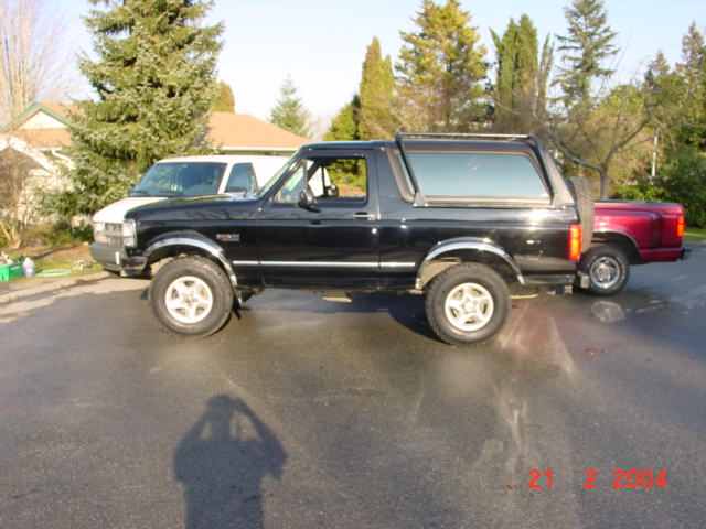 Black 1995 Ford Bronco parked next to a red pickup truck, side view