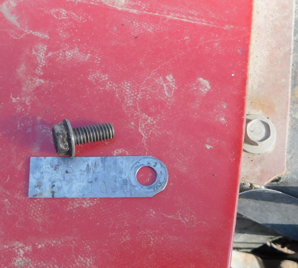Bolt and metal tag with numbers 'PGB W 1031' on a red surface