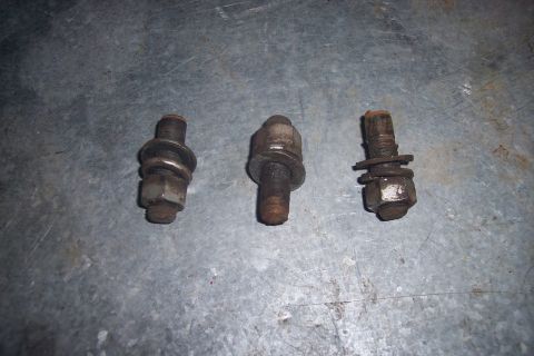 1973 Ford F-250 - Three used bolts with nuts and washers are laid out on a textured metal surface.