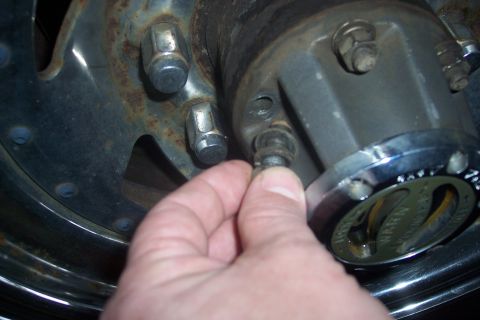 1973 Ford F-250 - A hand is shown removing a bolt from a Warn front hub assembly, likely during maintenance or repair.