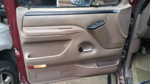 1996 Ford Bronco - The interior door panel of a 1996 Ford Bronco shows tan upholstery, power window controls, and a manual window crank.