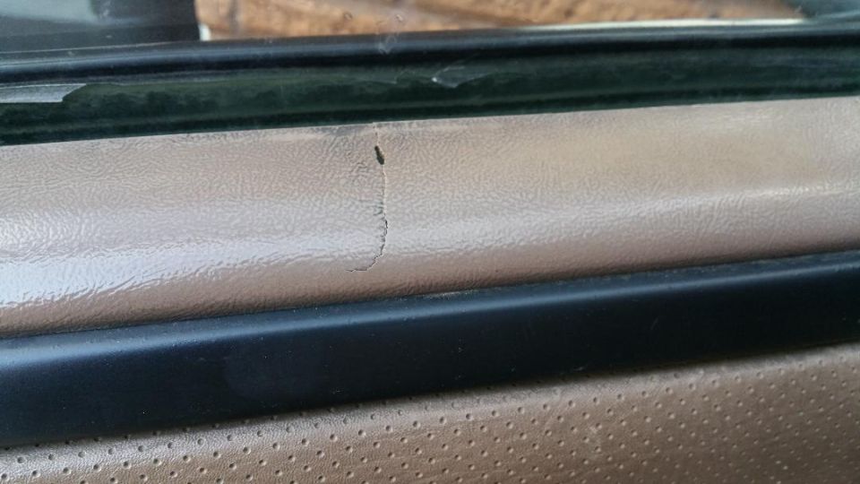 Tan interior door panel with a crack in the vinyl trim